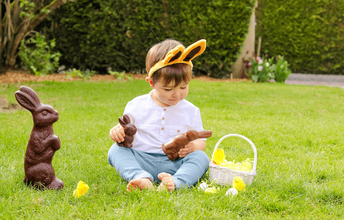 Cute little toddler child with bunny ears eating Easter chocolate outdoors by Kiwitanya